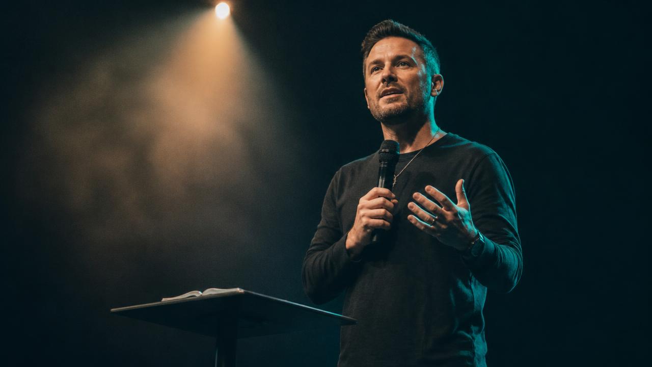 Pastor teaching on a dark stage under a warm spotlight